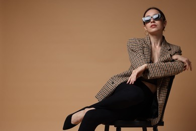 Photo of Beautiful woman in stylish outfit sitting on chair against beige background, space for text