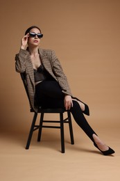 Photo of Beautiful woman in stylish outfit sitting on chair against beige background