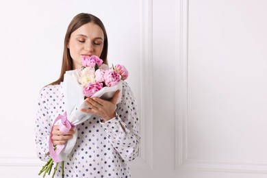 Photo of Woman with beautiful bouquet of peonies near white wall indoors, space for text
