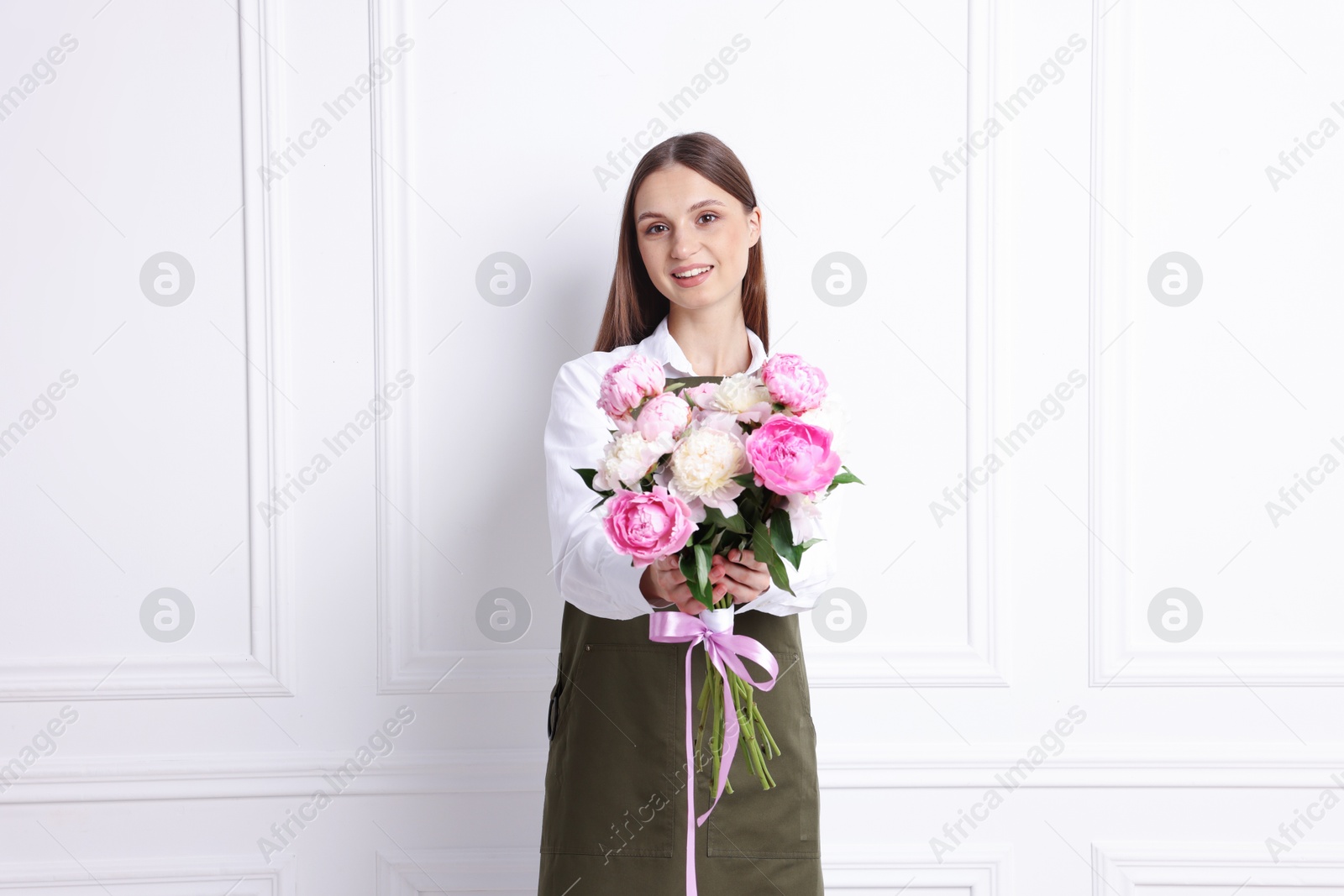 Florist with beautiful bouquet of peonies near white wall indoors Photo of Florist with beautiful bouquet of peonies near white wall indoors