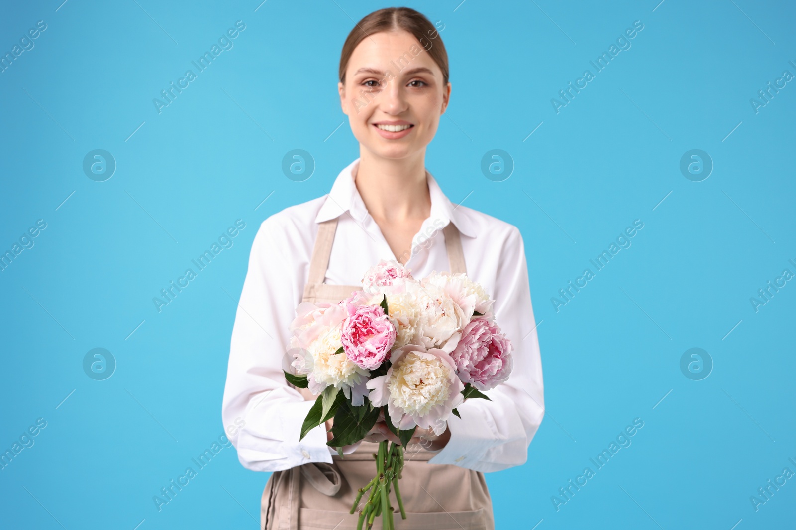 Florist with beautiful bouquet of peonies on light blue background Photo of Florist with beautiful bouquet of peonies on light blue background