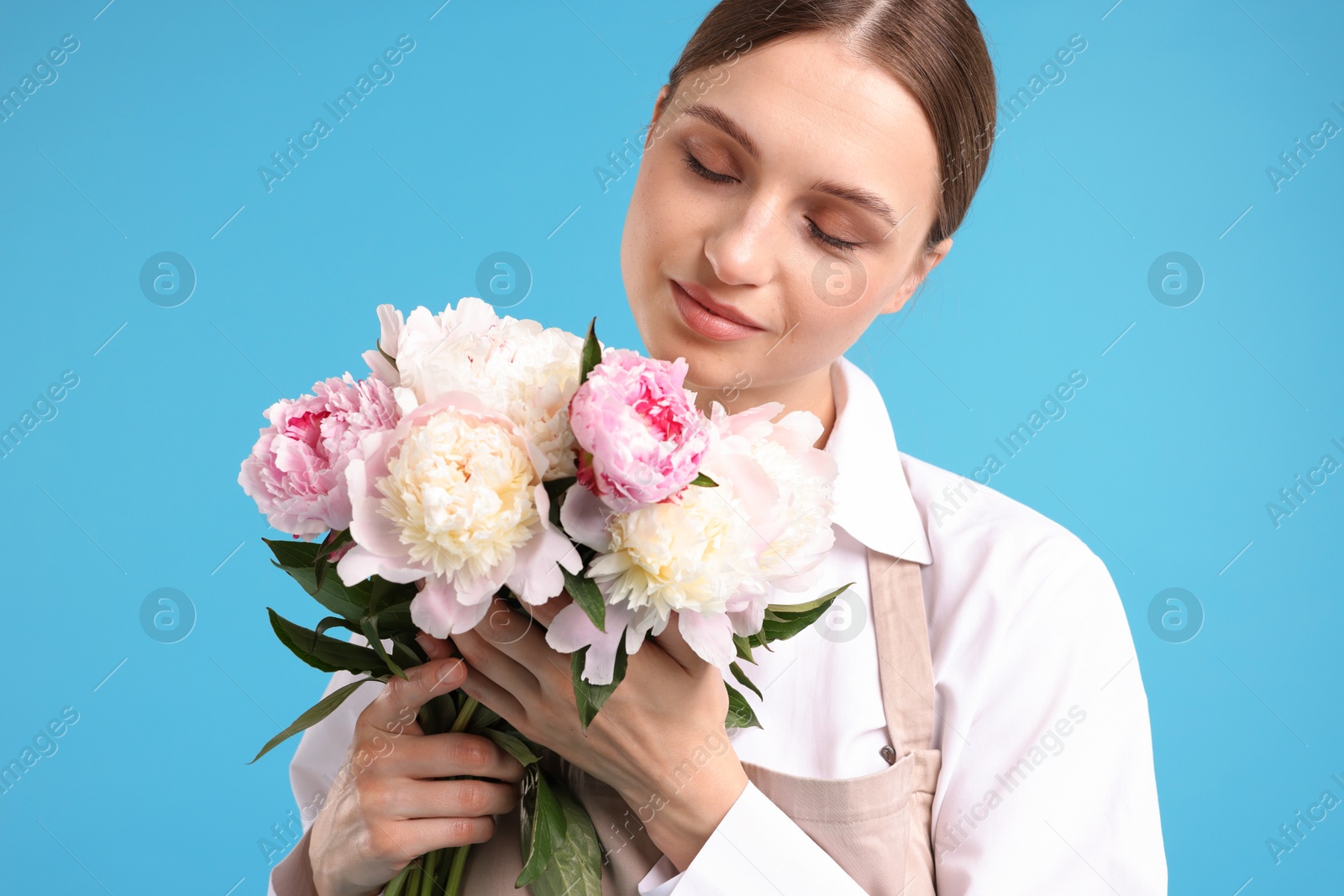 Florist with beautiful bouquet of peonies on light blue background Photo of Florist with beautiful bouquet of peonies on light blue background