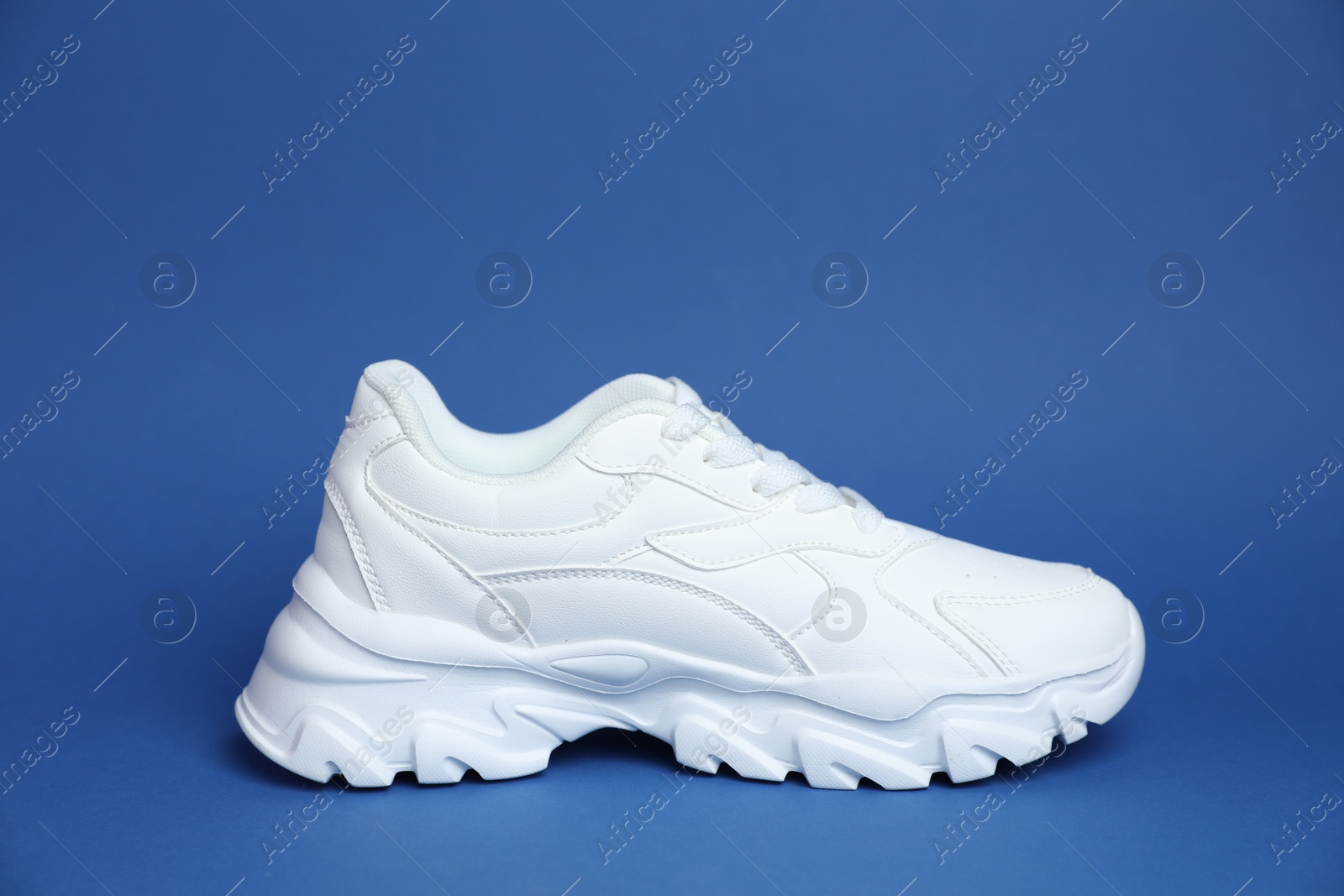 One stylish white sneaker on blue background Photo of One stylish white sneaker on blue background