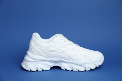 Photo of One stylish white sneaker on blue background