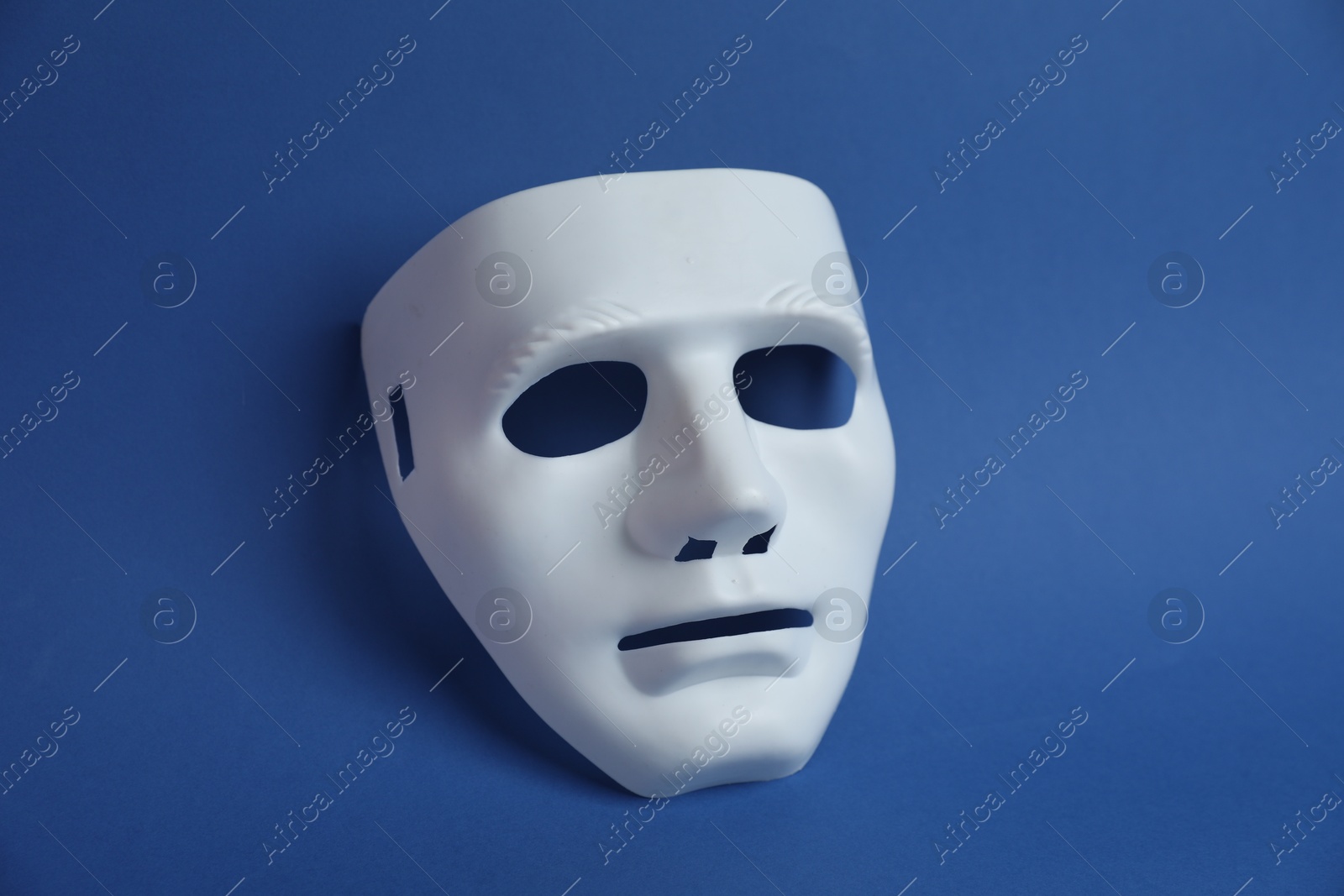 One white theatre mask on blue background, above view Photo of One white theatre mask on blue background, above view
