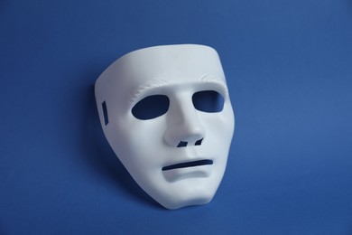 Photo of One white theatre mask on blue background, above view
