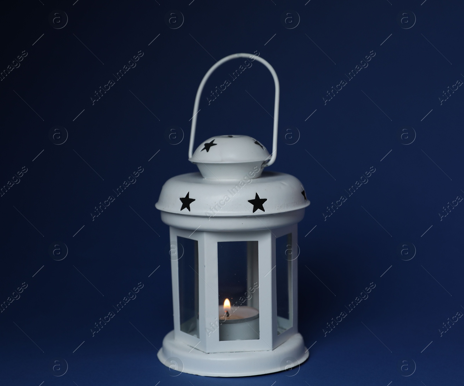 Beautiful white decorative lantern with burning candle on blue background Photo of Beautiful white decorative lantern with burning candle on blue background