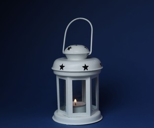 Photo of Beautiful white decorative lantern with burning candle on blue background