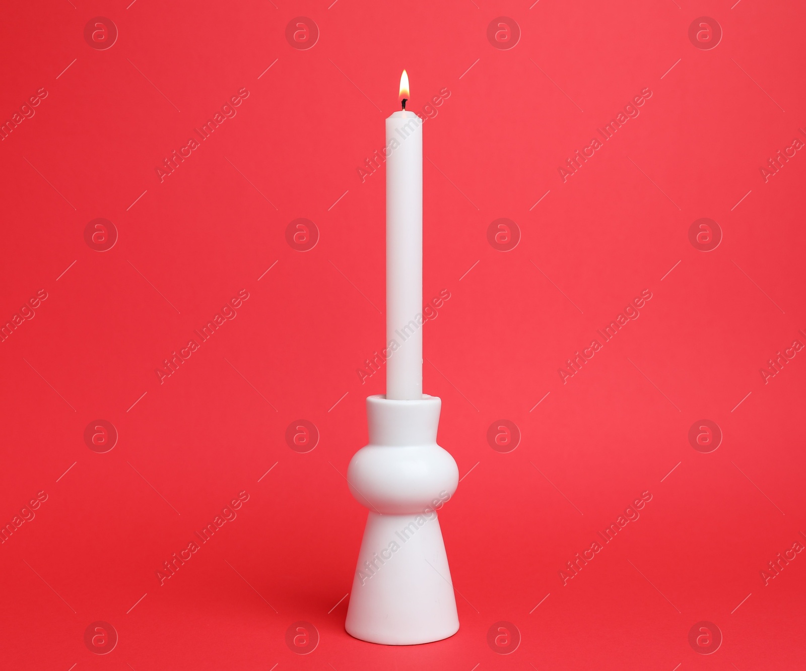 White candlestick with burning candle on red background Photo of White candlestick with burning candle on red background
