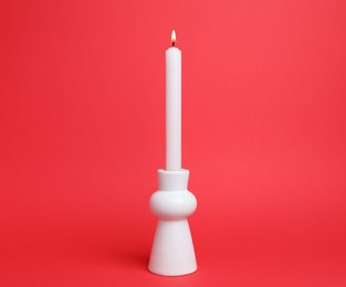 Photo of White candlestick with burning candle on red background