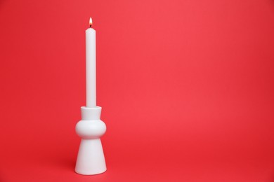 Photo of White candlestick with burning candle on red background, space for text