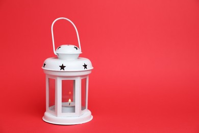 Photo of Beautiful white decorative lantern with burning candle on red background, space for text