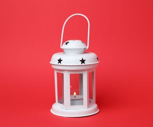 Photo of Beautiful white decorative lantern with burning candle on red background