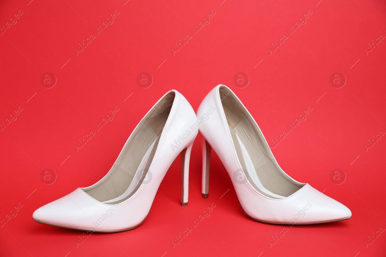 Pair of white high heeled shoes on red background Photo of Pair of white high heeled shoes on red background