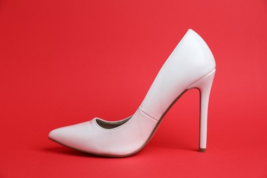 Photo of One white high heeled shoe on red background