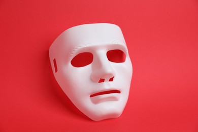 Photo of One white theatre mask on red background, above view
