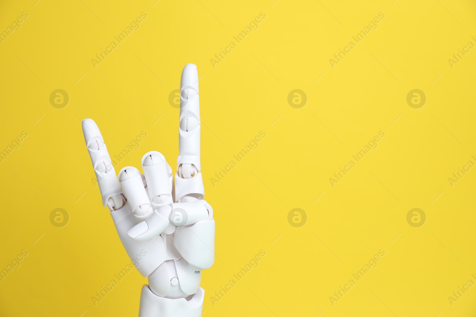 White mannequin hand making rock gesture on yellow background, space for text Photo of White mannequin hand making rock gesture on yellow background, space for text