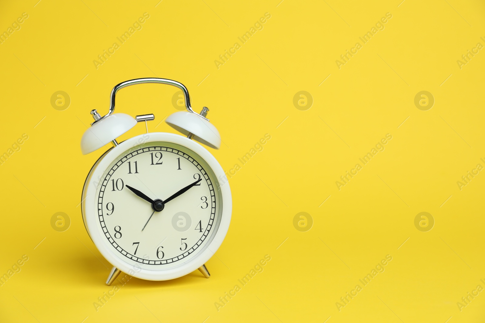One white alarm clock on yellow background, space for text Photo of One white alarm clock on yellow background, space for text
