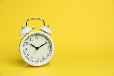 Photo of One white alarm clock on yellow background, space for text
