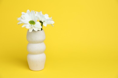 Photo of Beautiful white chrysanthemum flowers in vase on yellow background, space for text