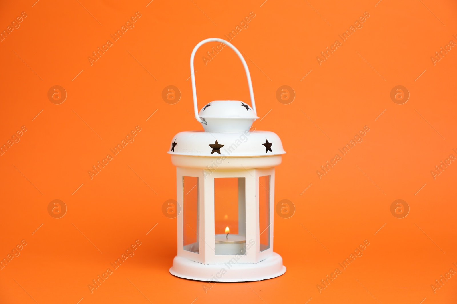 Beautiful white decorative lantern with burning candle on orange background Photo of Beautiful white decorative lantern with burning candle on orange background