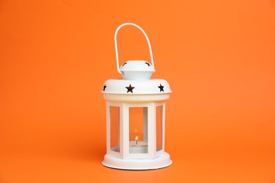 Photo of Beautiful white decorative lantern with burning candle on orange background