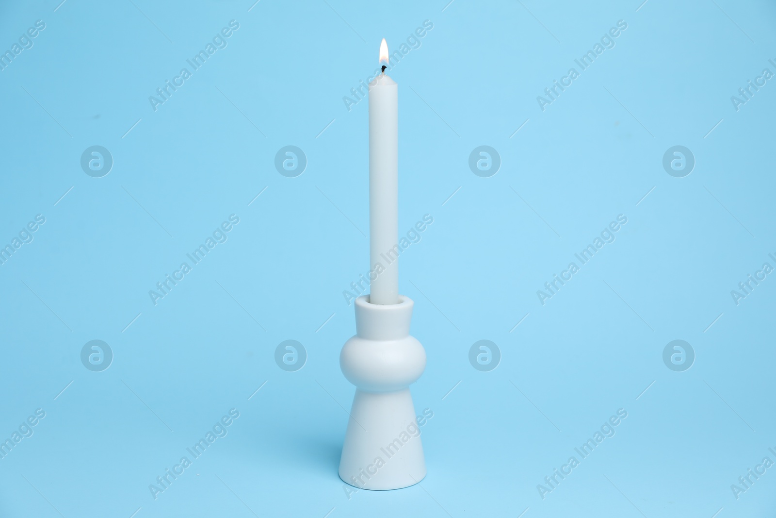 White candlestick with burning candle on light blue background Photo of White candlestick with burning candle on light blue background