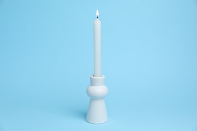 Photo of White candlestick with burning candle on light blue background