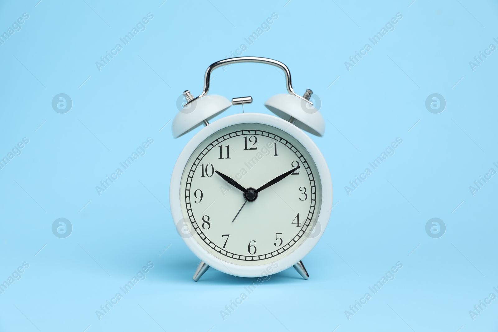 One white alarm clock on light blue background Photo of One white alarm clock on light blue background