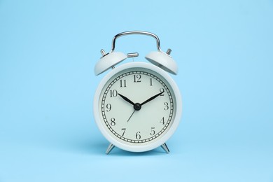 Photo of One white alarm clock on light blue background