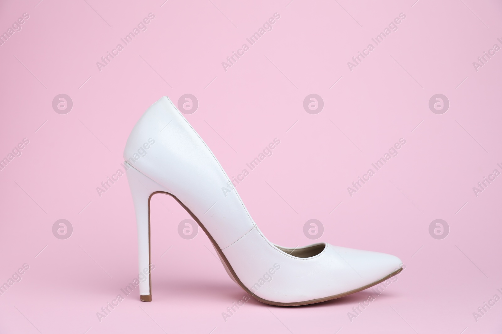 One white high heeled shoe on pink background Photo of One white high heeled shoe on pink background