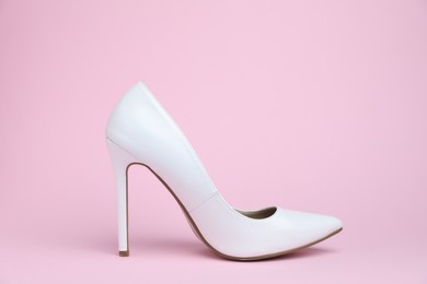 Photo of One white high heeled shoe on pink background