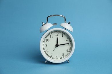 Photo of One white alarm clock on light blue background
