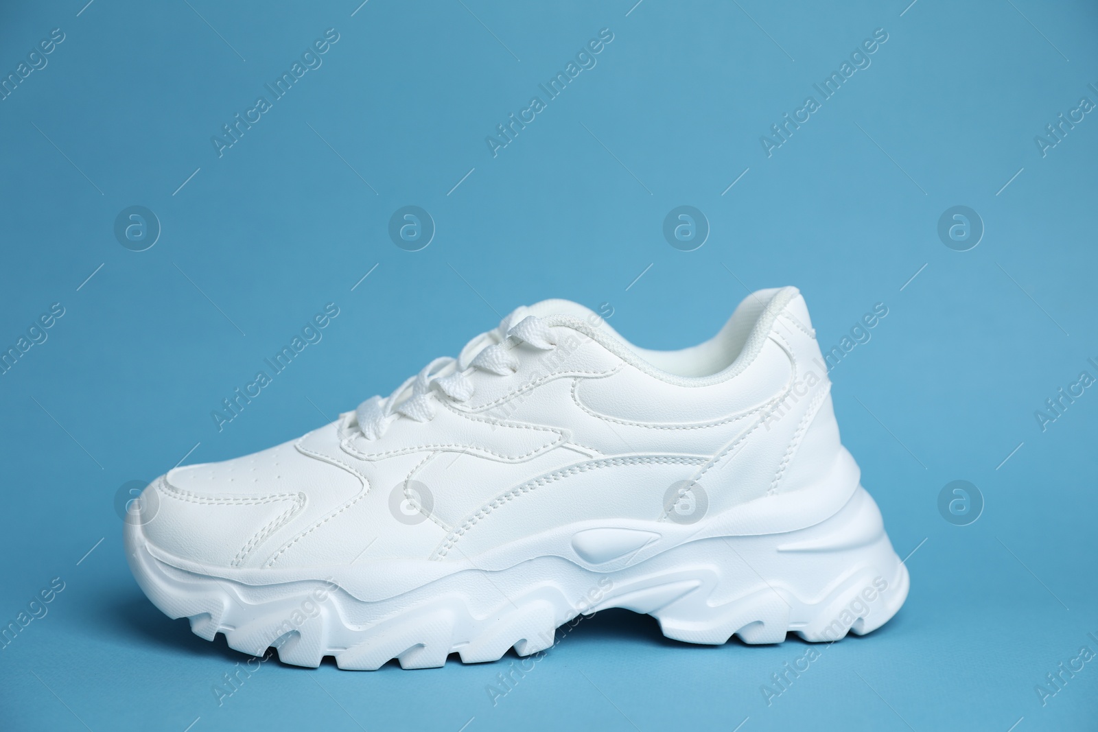 One stylish white sneaker on light blue background Photo of One stylish white sneaker on light blue background
