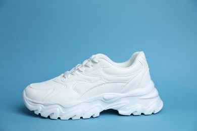 Photo of One stylish white sneaker on light blue background
