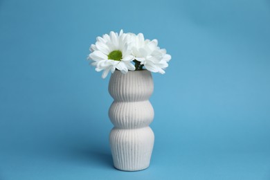 Photo of Beautiful white chrysanthemum flowers in vase on light blue background