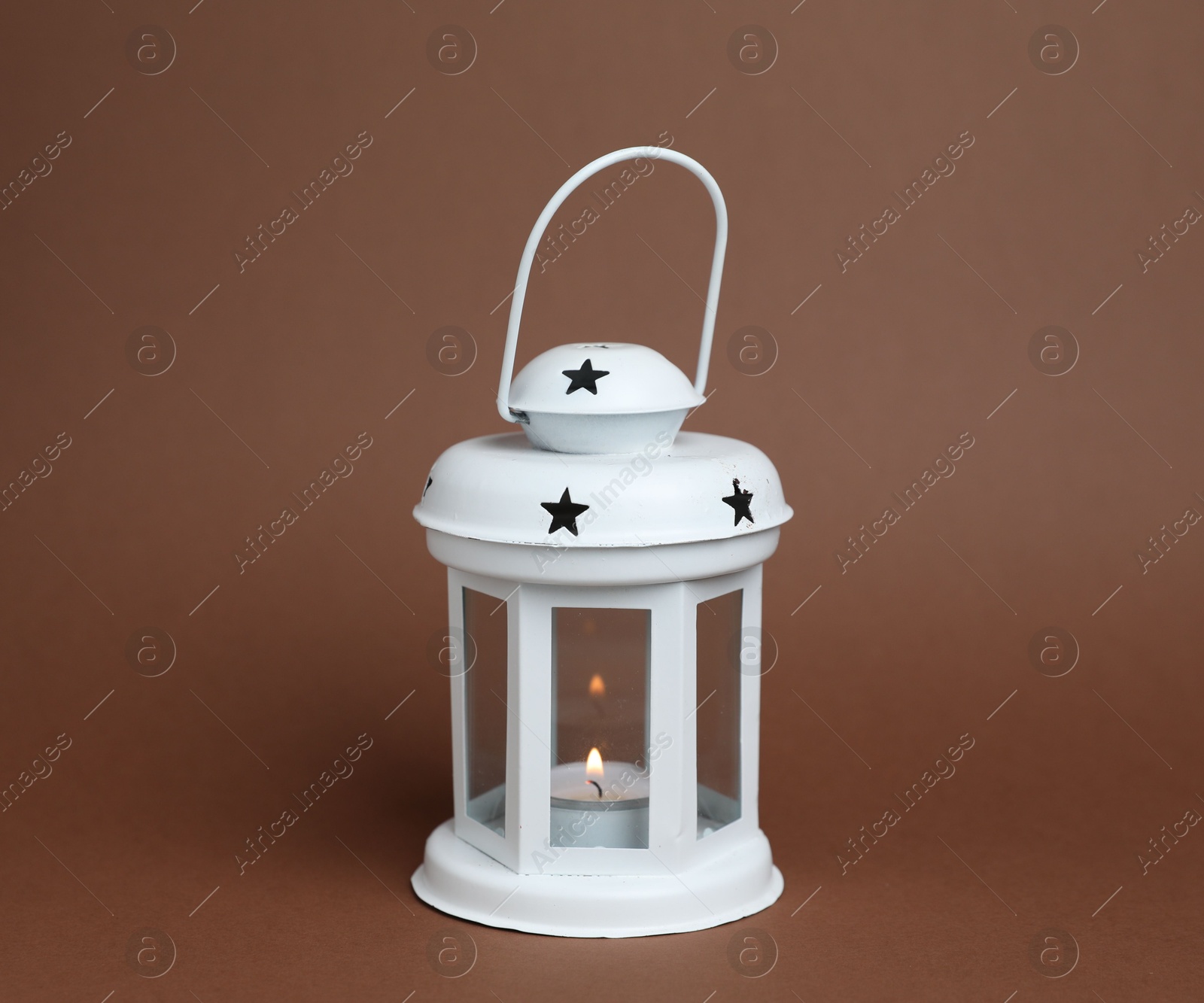 Beautiful white decorative lantern with burning candle on brown background Photo of Beautiful white decorative lantern with burning candle on brown background