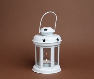 Photo of Beautiful white decorative lantern with burning candle on brown background