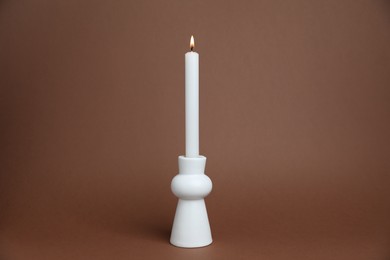 Photo of White candlestick with burning candle on brown background