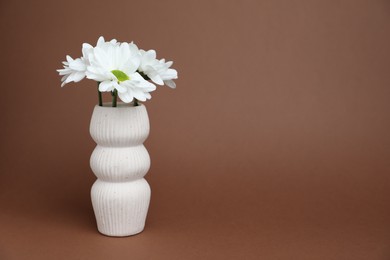 Photo of Beautiful white chrysanthemum flowers in vase on brown background, space for text