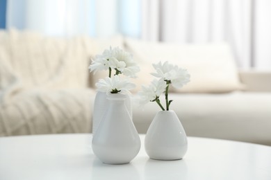 Photo of Beautiful chrysanthemum flowers in vases on white table indoors
