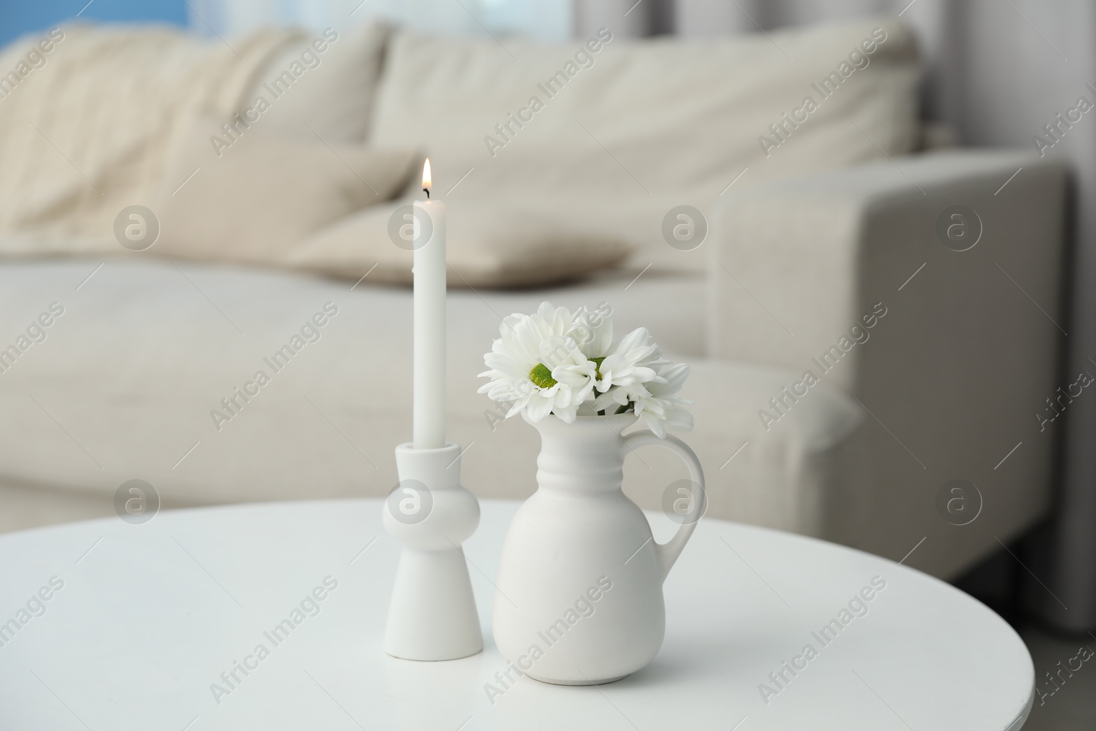 Beautiful chrysanthemum flowers in vase and burning candle on white table indoors Photo of Beautiful chrysanthemum flowers in vase and burning candle on white table indoors