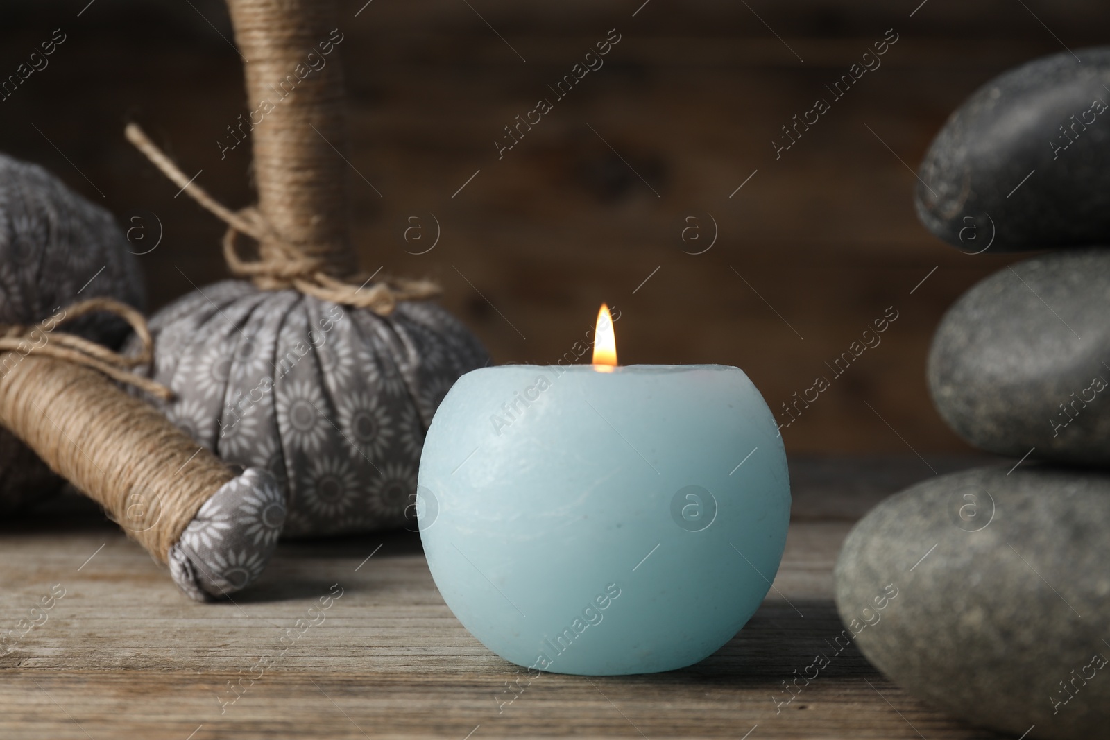 Photo of Spa stones, herbal bags and burning candle on wooden table, closeup