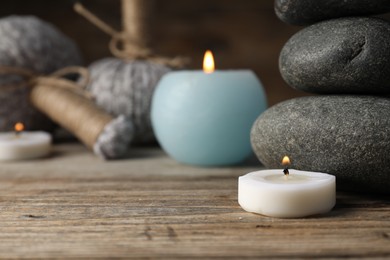 Photo of Spa stones, herbal bags and burning candles on wooden table, closeup