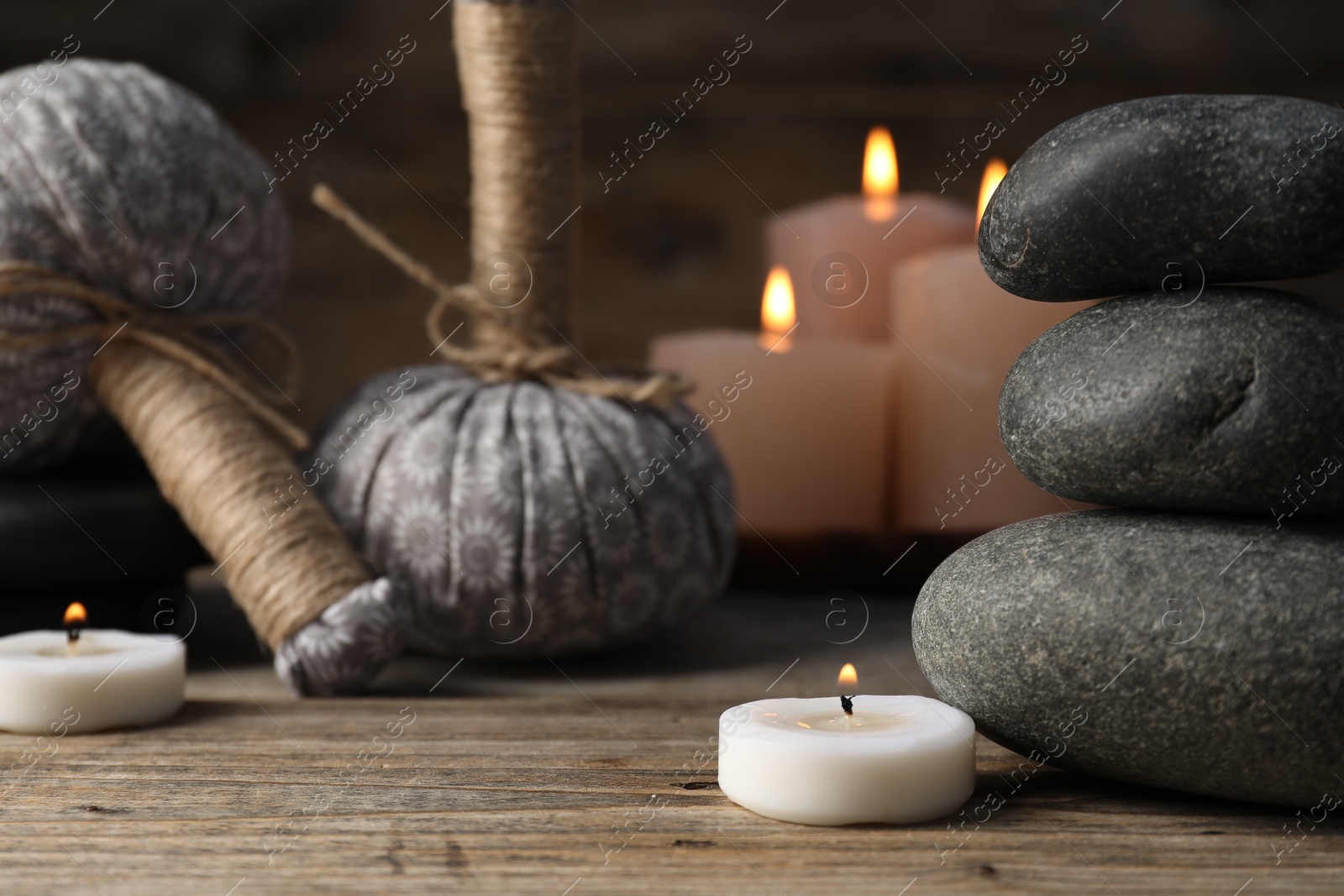 Spa stones, herbal bags and burning candles on wooden table, closeup Photo of Spa stones, herbal bags and burning candles on wooden table, closeup