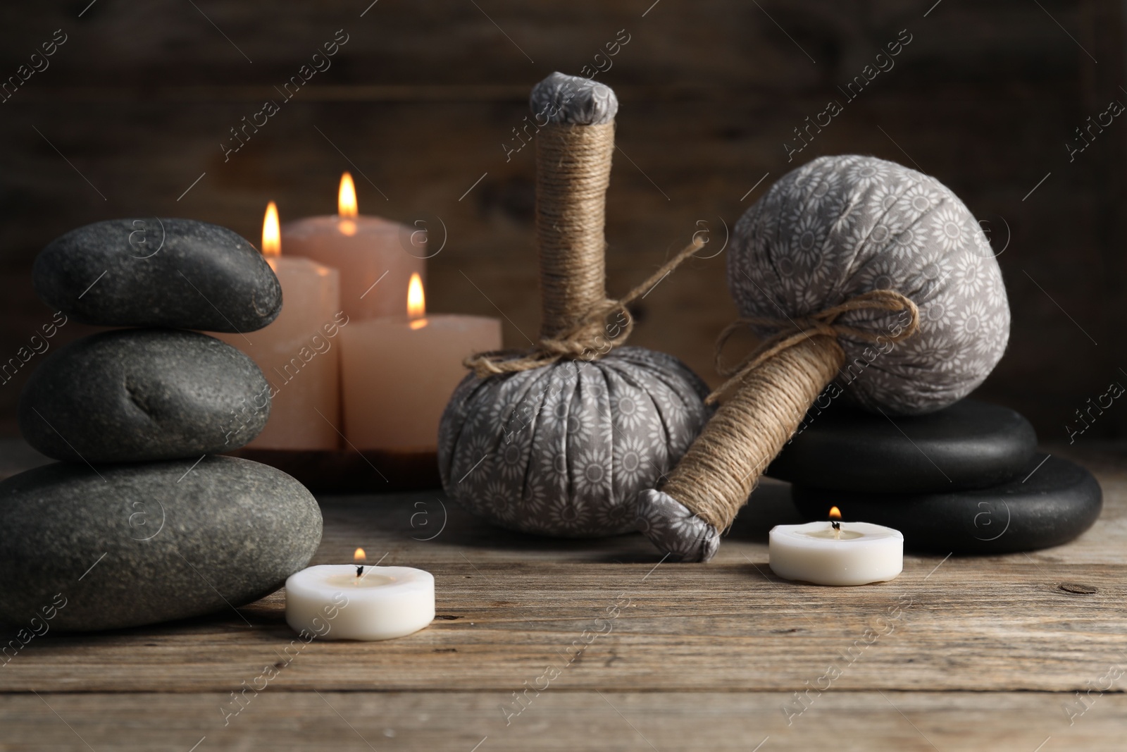 Spa stones, herbal bags and burning candles on wooden table, closeup Photo of Spa stones, herbal bags and burning candles on wooden table, closeup