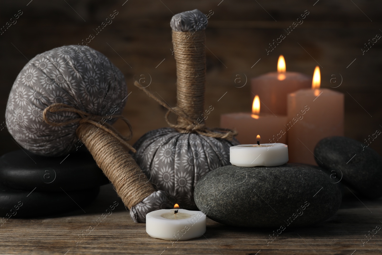 Spa stones, herbal bags and burning candles on wooden table, closeup Photo of Spa stones, herbal bags and burning candles on wooden table, closeup