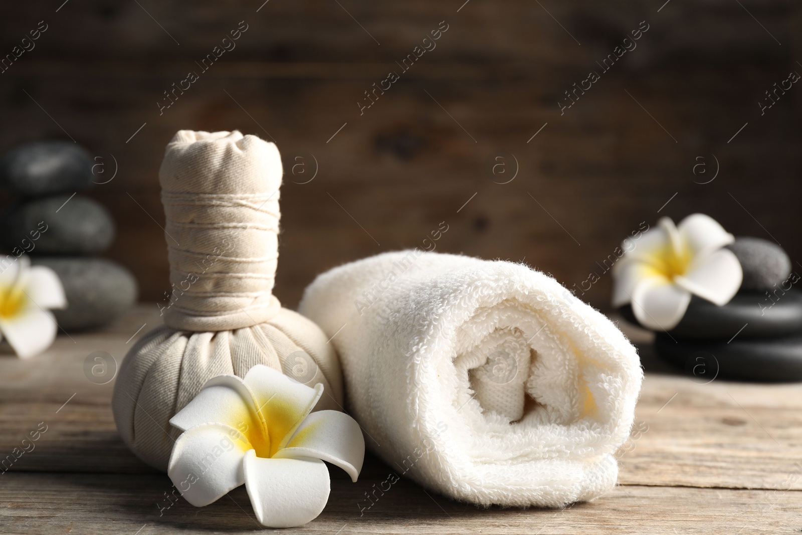 Herbal bag, towel, spa stones and plumeria flowers on wooden table, closeup Photo of Herbal bag, towel, spa stones and plumeria flowers on wooden table, closeup