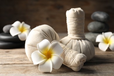 Photo of Herbal bags, spa stones and plumeria flowers on wooden table, closeup