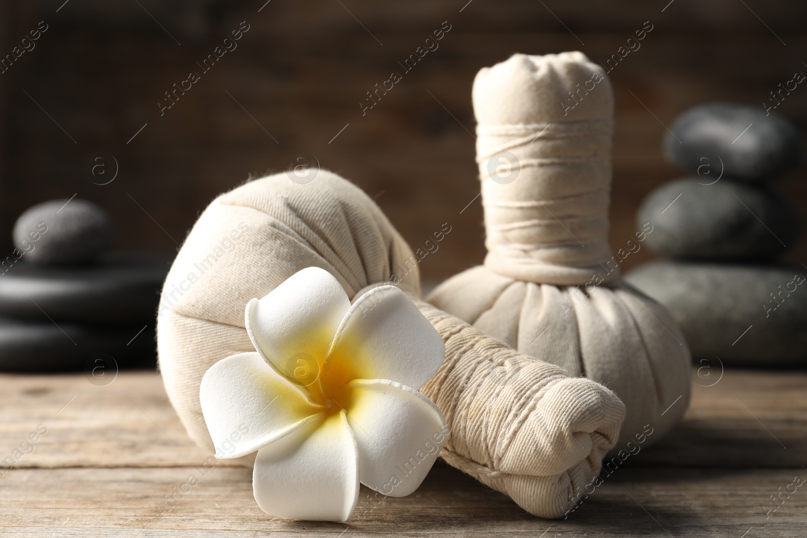 Herbal bags, spa stones and plumeria flower on wooden table, closeup Photo of Herbal bags, spa stones and plumeria flower on wooden table, closeup